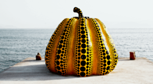 Yayoi Kusama Pumpkin Sculpture on a pier with water in the background.